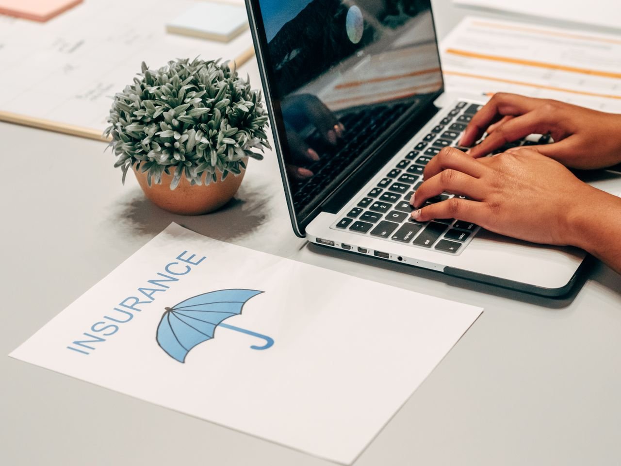 Mastering the First Impression: Your intriguing post title goes here Hands typing on a laptop at a desk with an insurance paper and plant, suggesting a work environment.